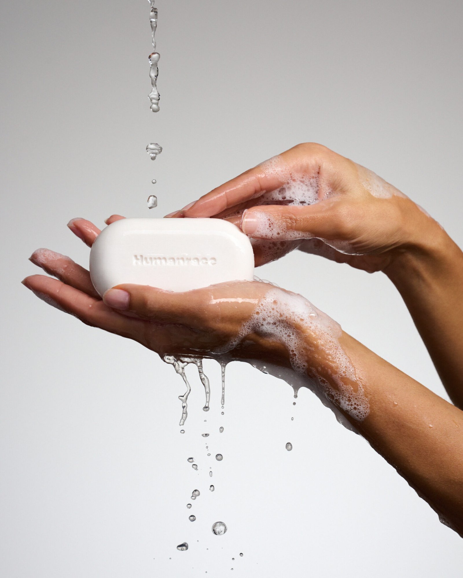 Kvindelig hånd holder i en sæbebar og der er skum og vandplask